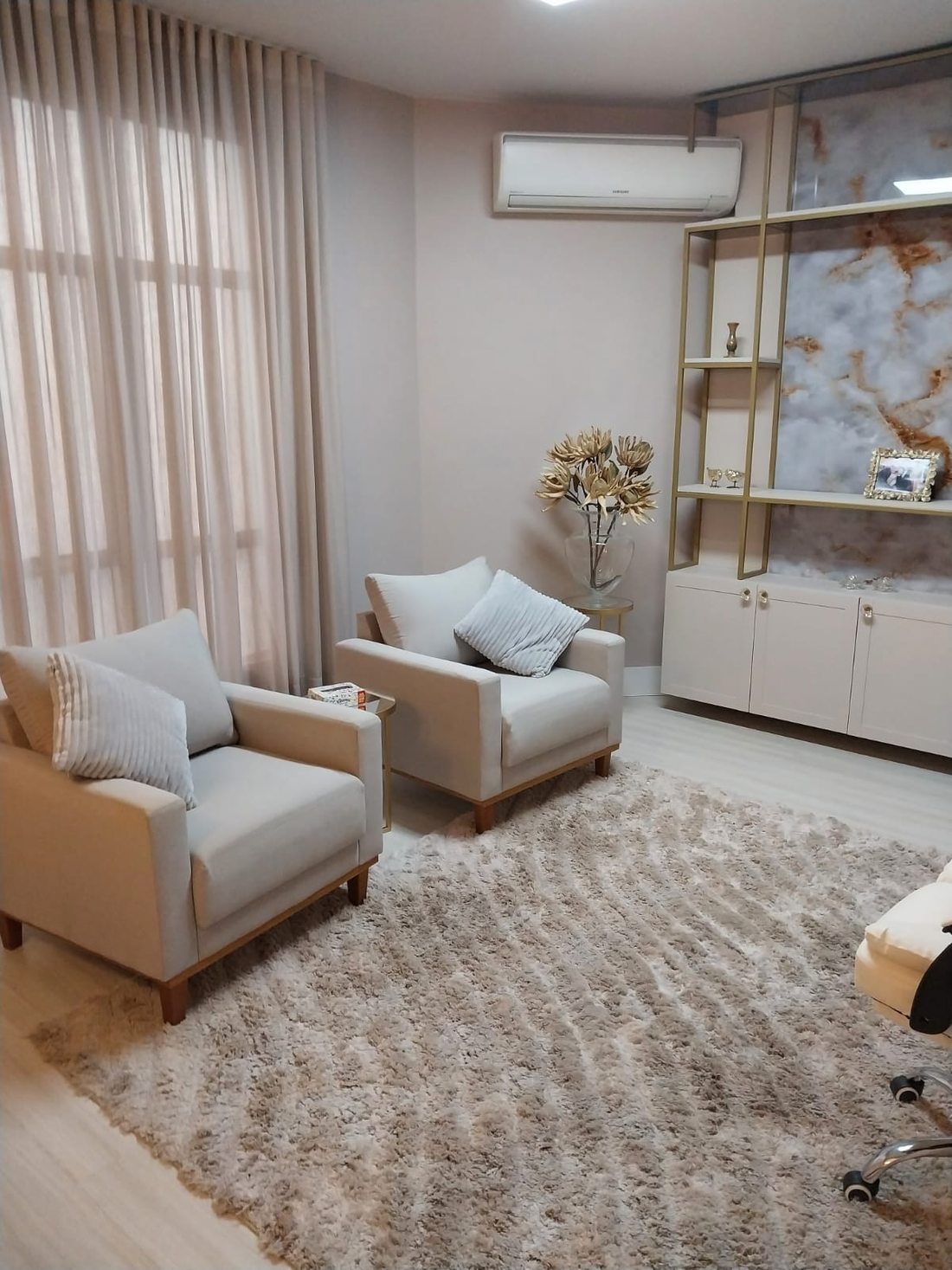 Sala de atendimento com poltrona, armário claro e arranjo de flores